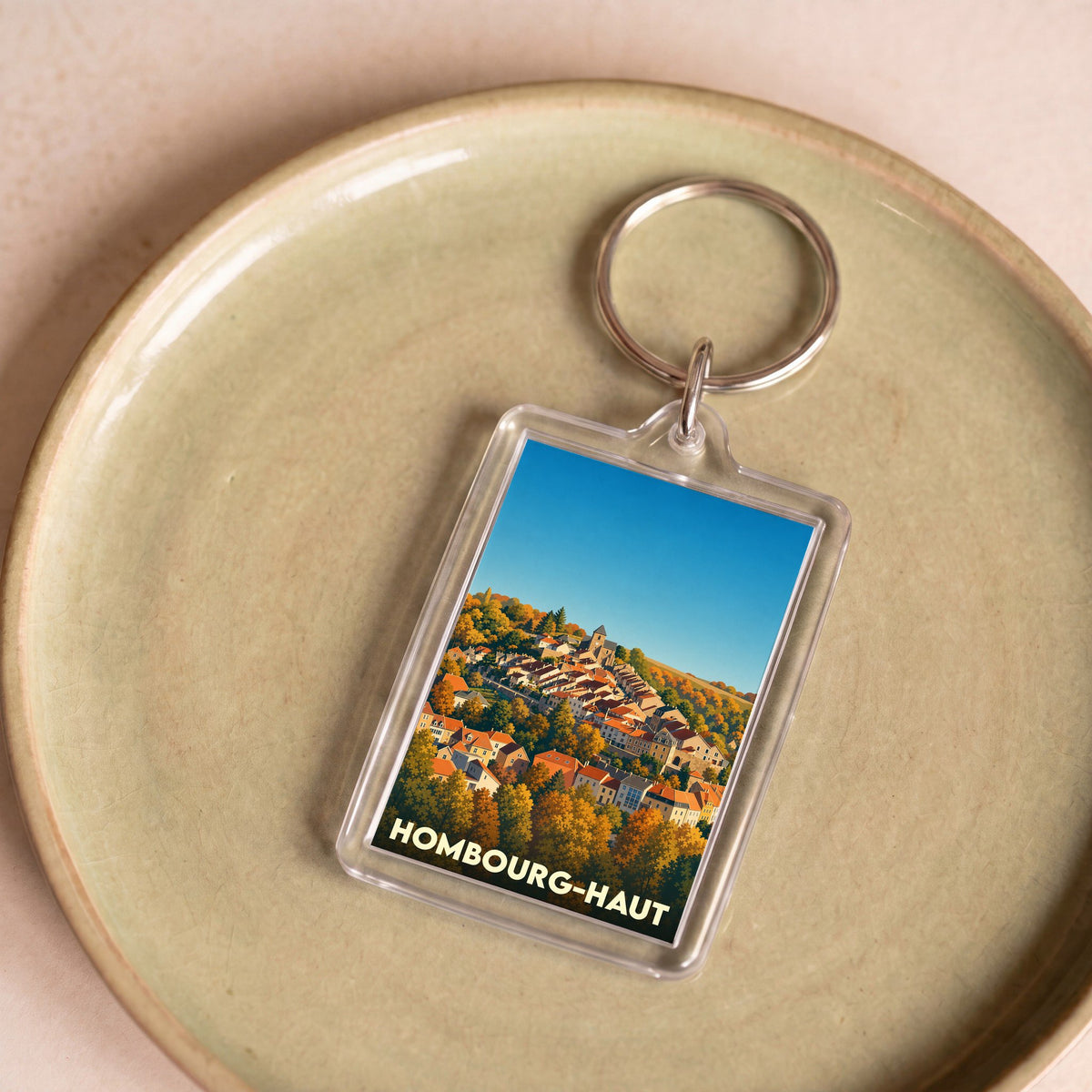 Porte-clés souvenir de la ville de Hombourg-Haut avec une illustration stylisée de son paysage urbain automnal.