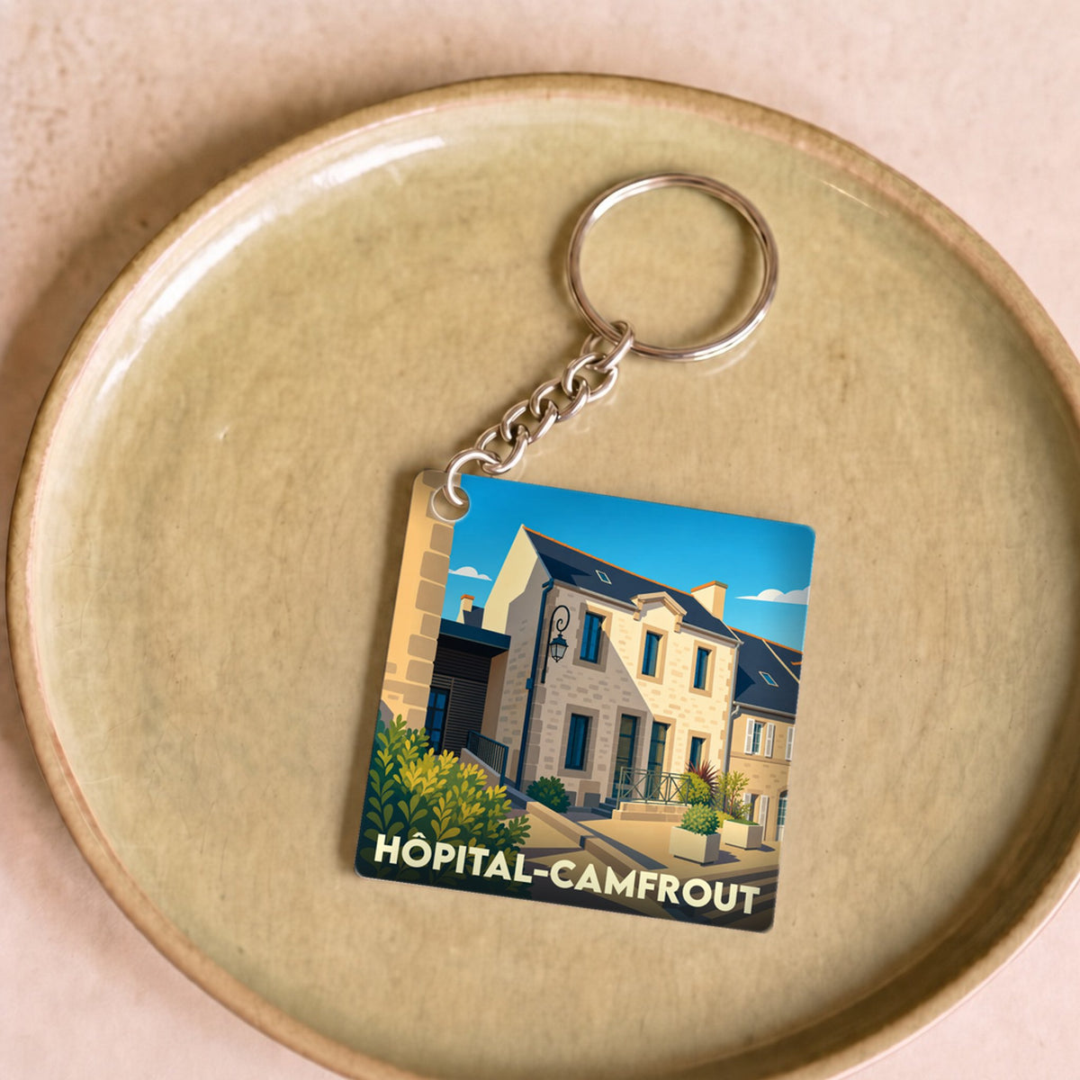Porte-clés souvenir de la ville de Hôpital-Camfrout avec une illustration stylisée d'une rue ensoleillée.