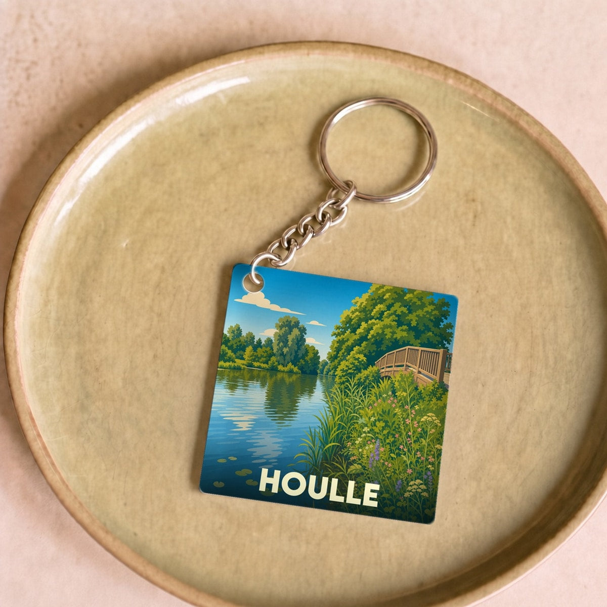 Porte-clés souvenir de la ville de Houlle avec une illustration stylisée représentant un paysage de rivière.