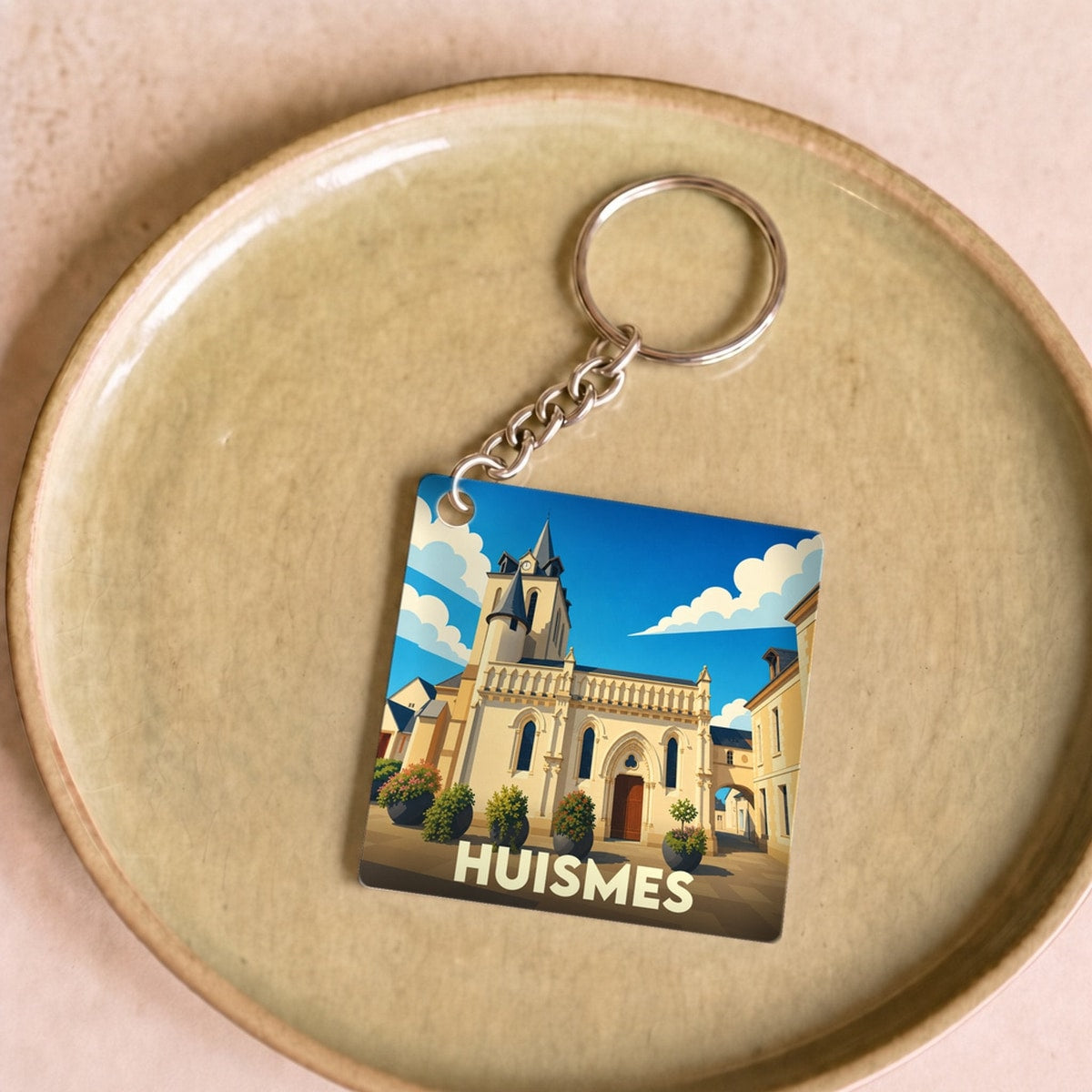 Porte-clés souvenir de la ville de Huismes avec une illustration stylisée de son église sous un ciel bleu.