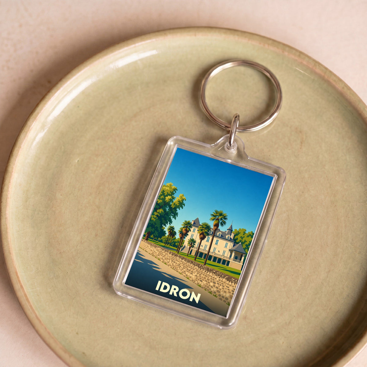 Porte-clés souvenir de la ville d'Idron avec une illustration stylisée d'un château et de palmiers.