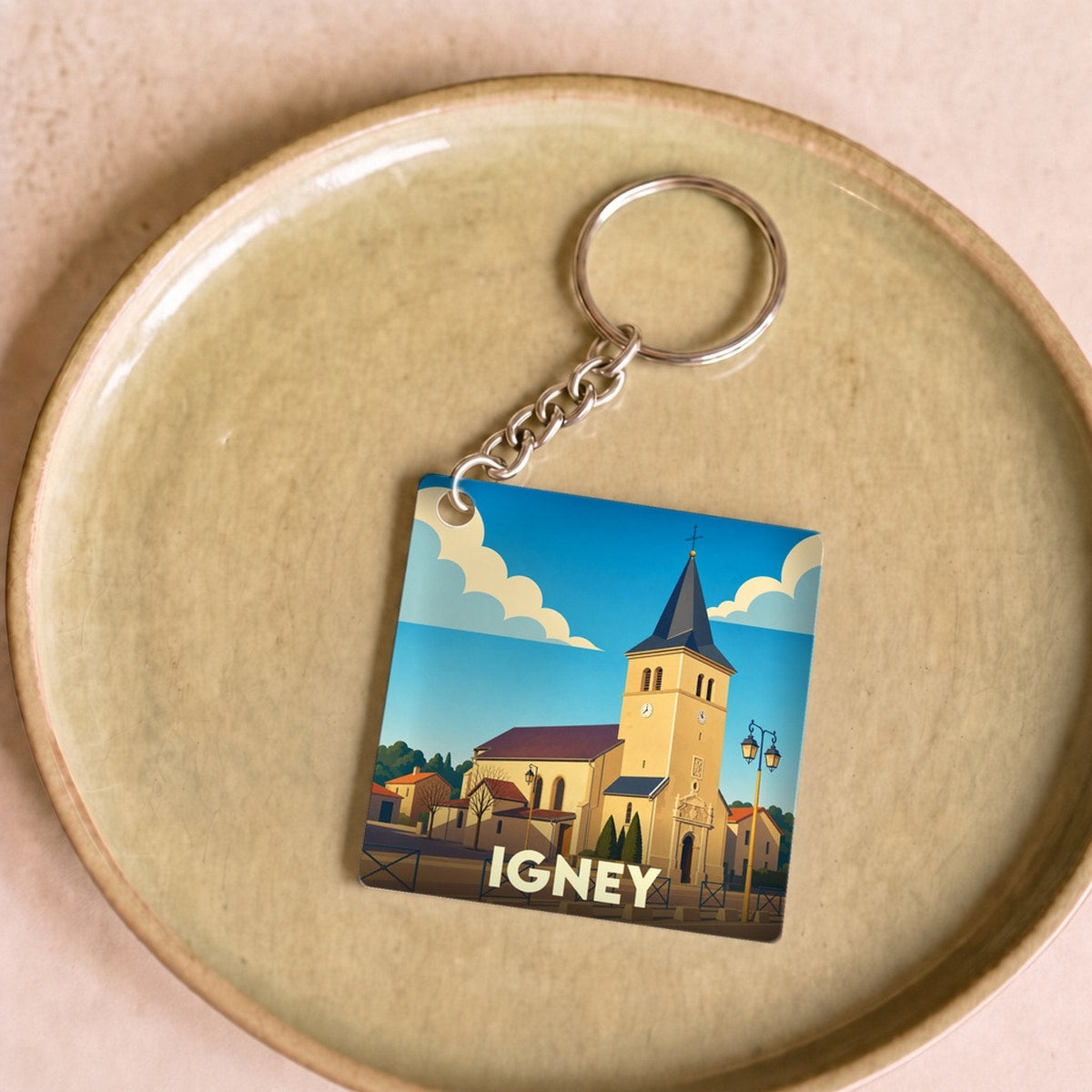 Porte-clés souvenir de la ville d'Igney avec une illustration stylisée de son église sous un ciel bleu.