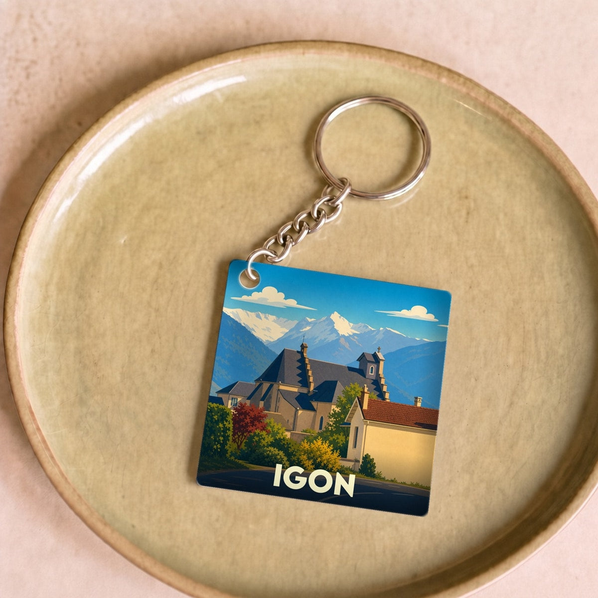 Porte-clés souvenir de la ville d'Igon avec une illustration stylisée des montagnes et de l'église locale.