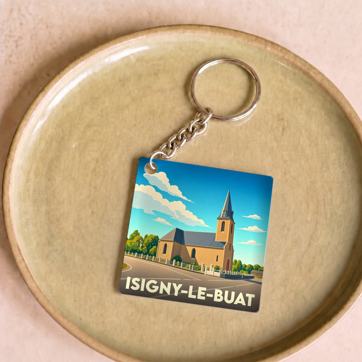 Porte-clés souvenir de la ville d'Isigny-le-Buat avec une illustration stylisée de son église.