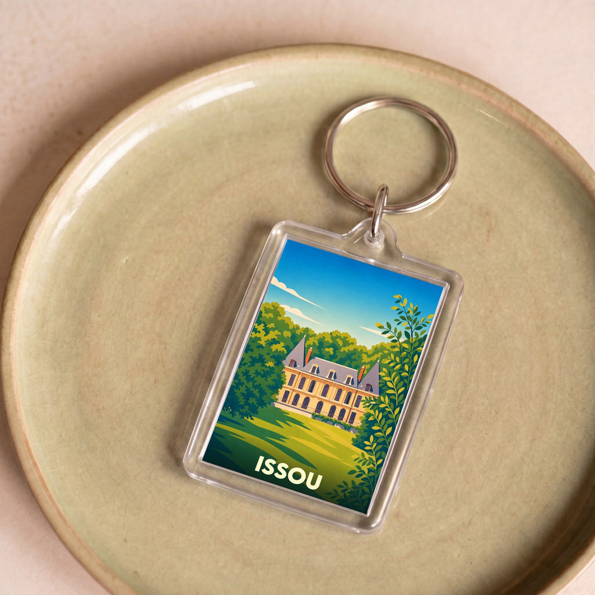Porte-clés souvenir de la ville d'Issou avec une illustration stylisée d'un château entouré de verdure.