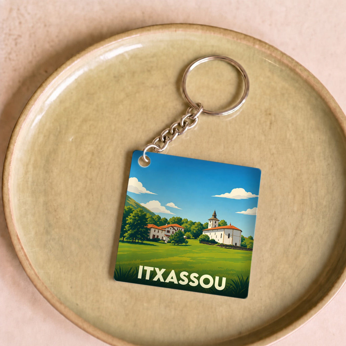 Porte-clés souvenir de la ville d'Itxassou avec une illustration stylisée d'un paysage basque.
