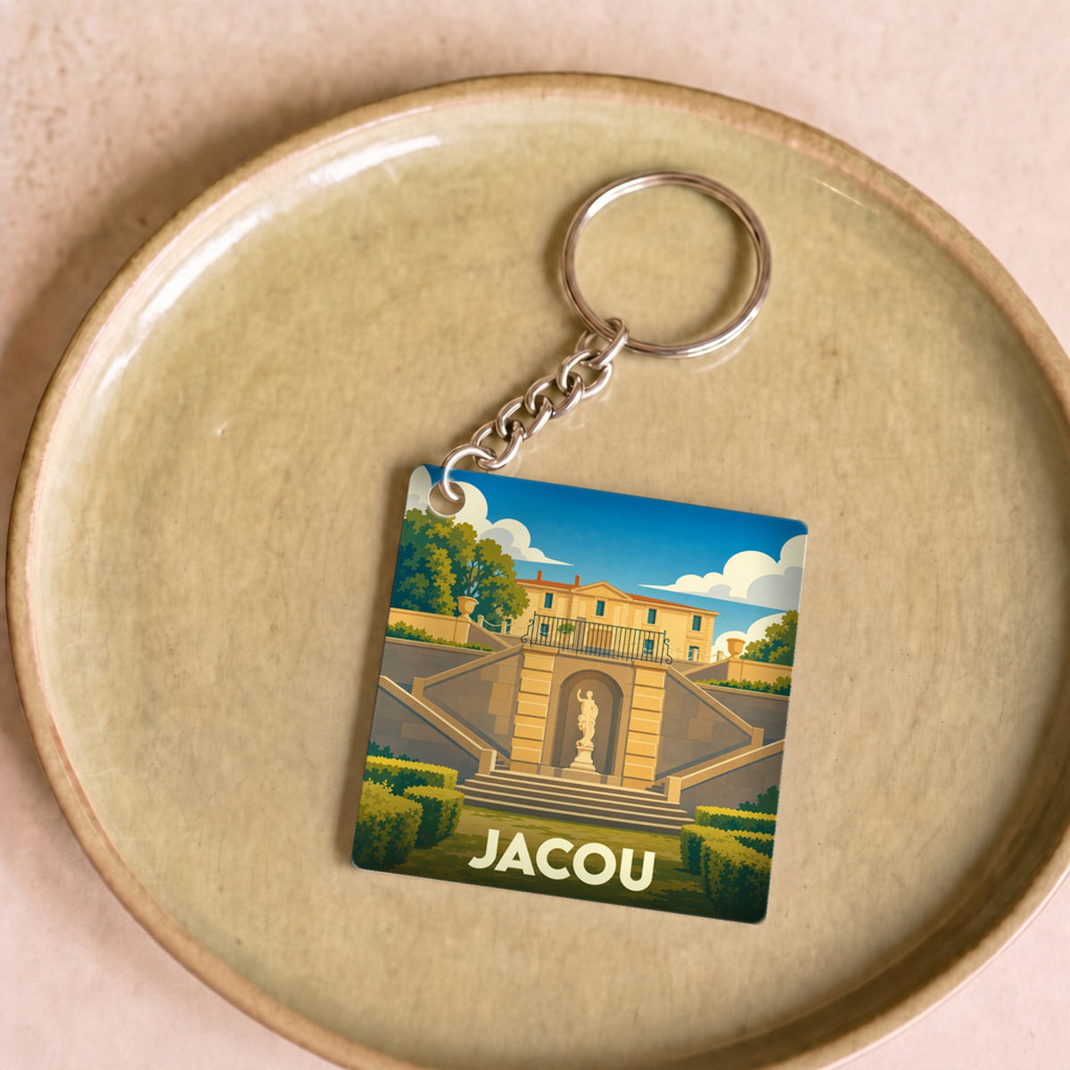 Porte-clés souvenir de la ville de Jacou avec une illustration stylisée d'un domaine historique.