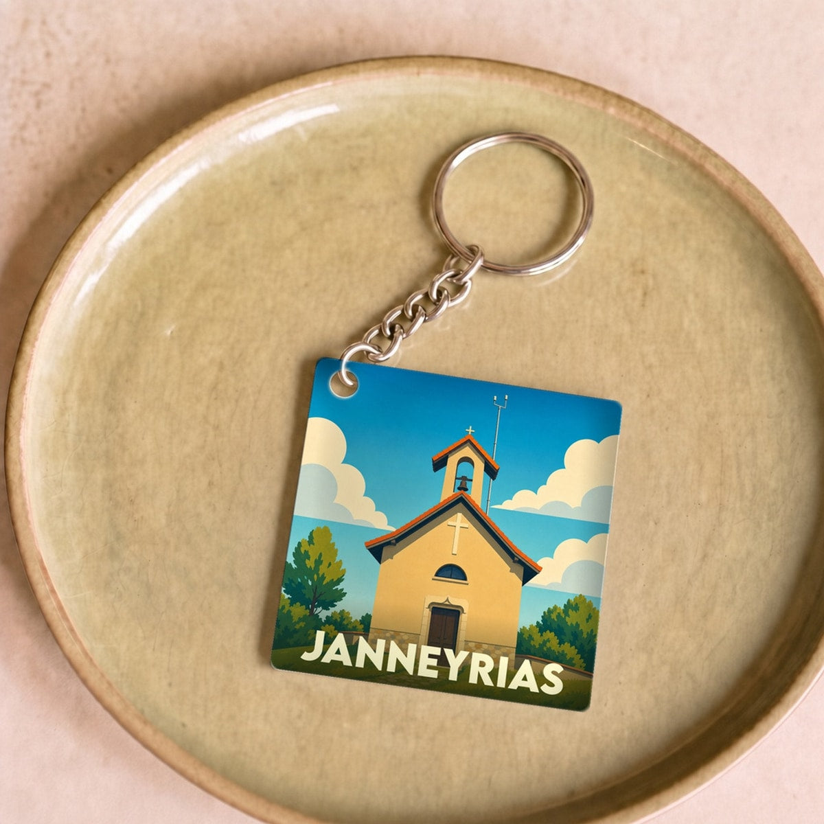 Porte-clés souvenir de la ville de Janneyrias avec une illustration stylisée d'une petite église sous un ciel bleu.