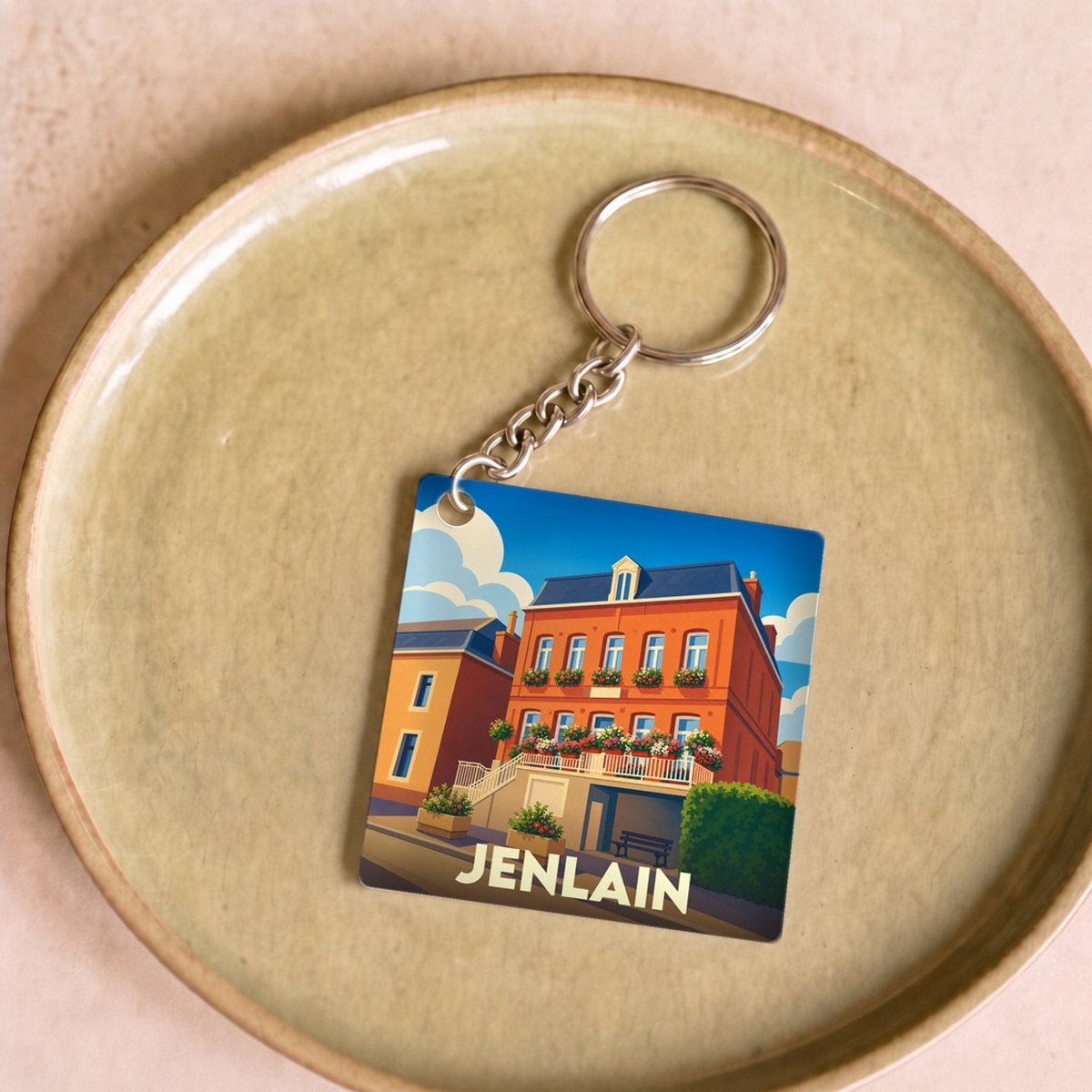 Porte-clés souvenir de la ville de Jenlain avec une illustration stylisée d'un bâtiment fleuri.
