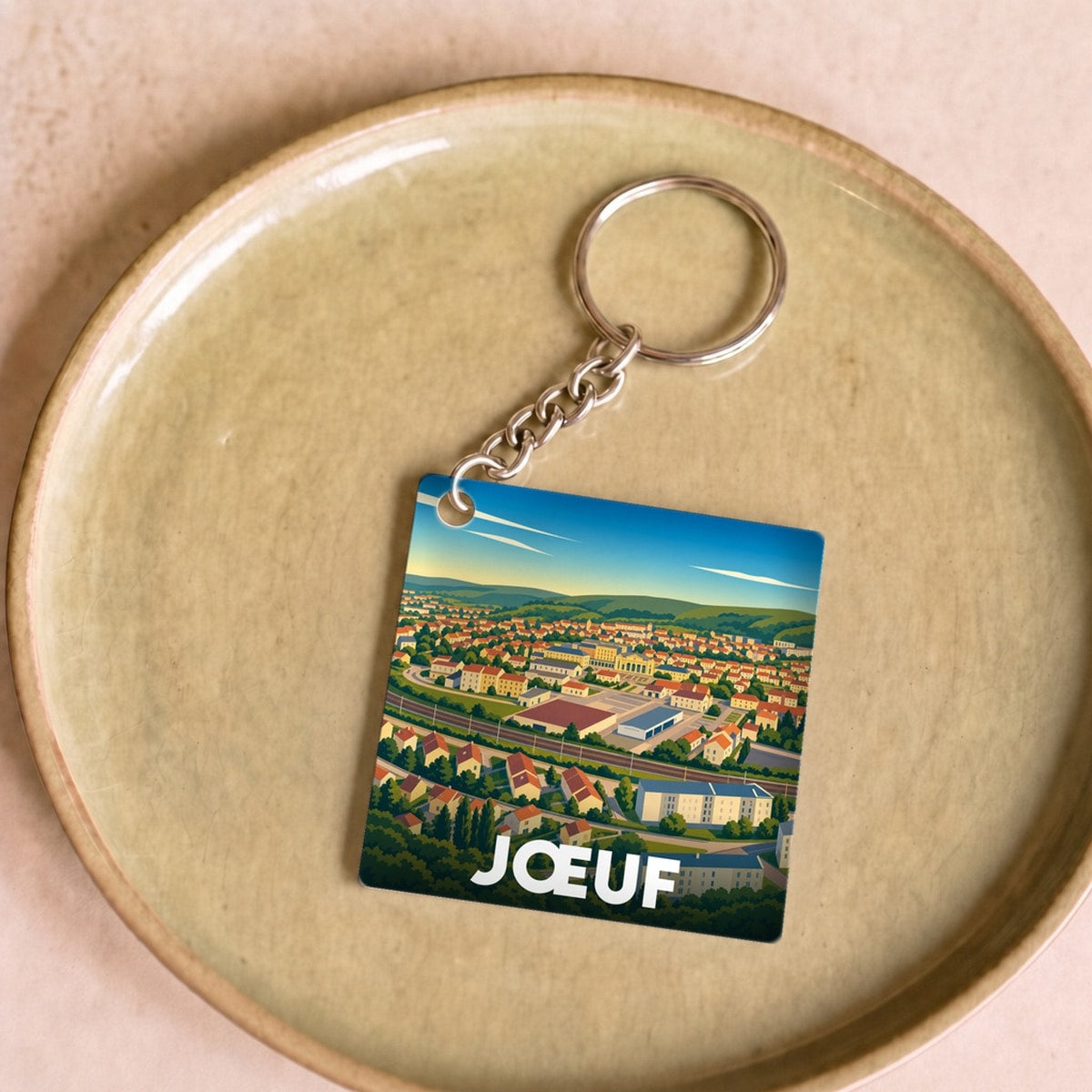 Porte-clés souvenir de la ville de Jœuf arborant une illustration paysagère stylisée.