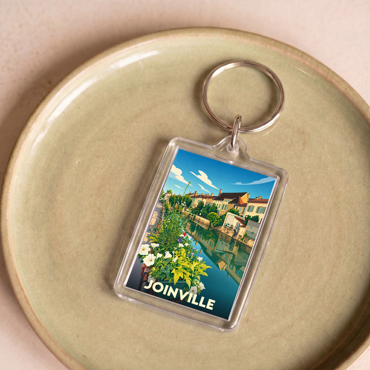 Porte-clés souvenir de la ville de Joinville avec une illustration stylisée d'un canal fleuri.