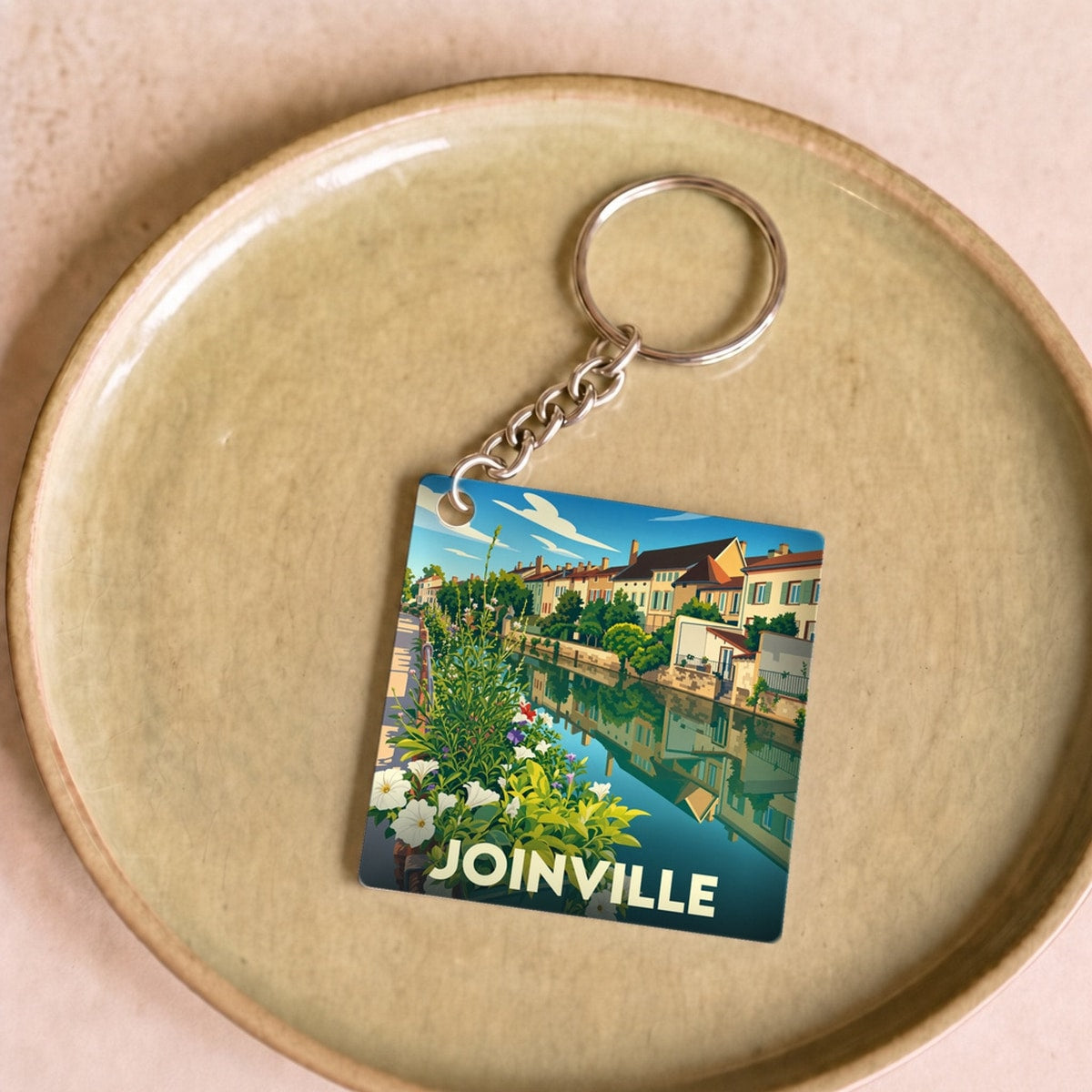 Porte-clés souvenir de la ville de Joinville avec une illustration stylisée d'un canal bordé de maisons et de fleurs.