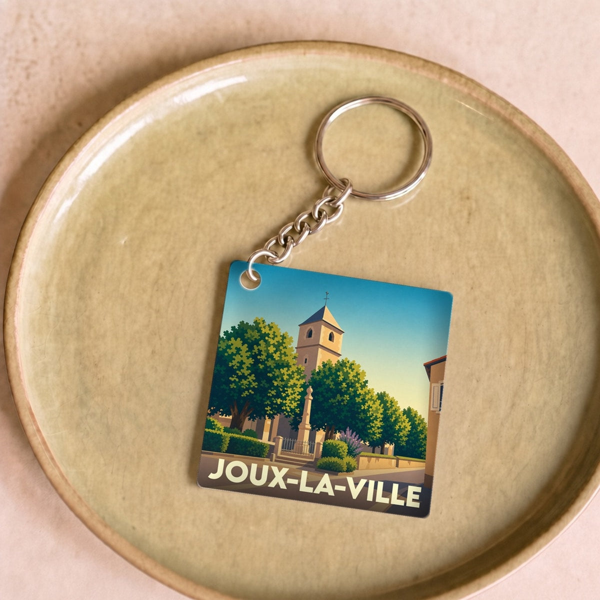 Porte-clés souvenir de Joux-la-Ville avec une illustration stylisée d'une église et d'une place arborée.