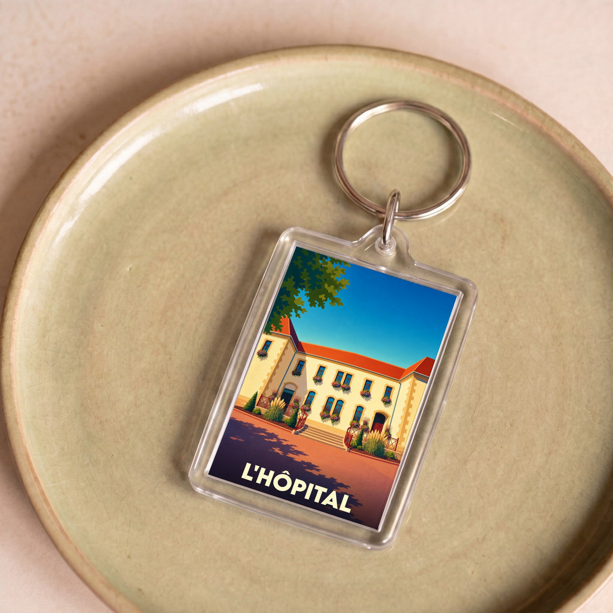 Porte-clés souvenir de la ville de L'Hôpital avec une illustration stylisée d'un bâtiment fleuri.