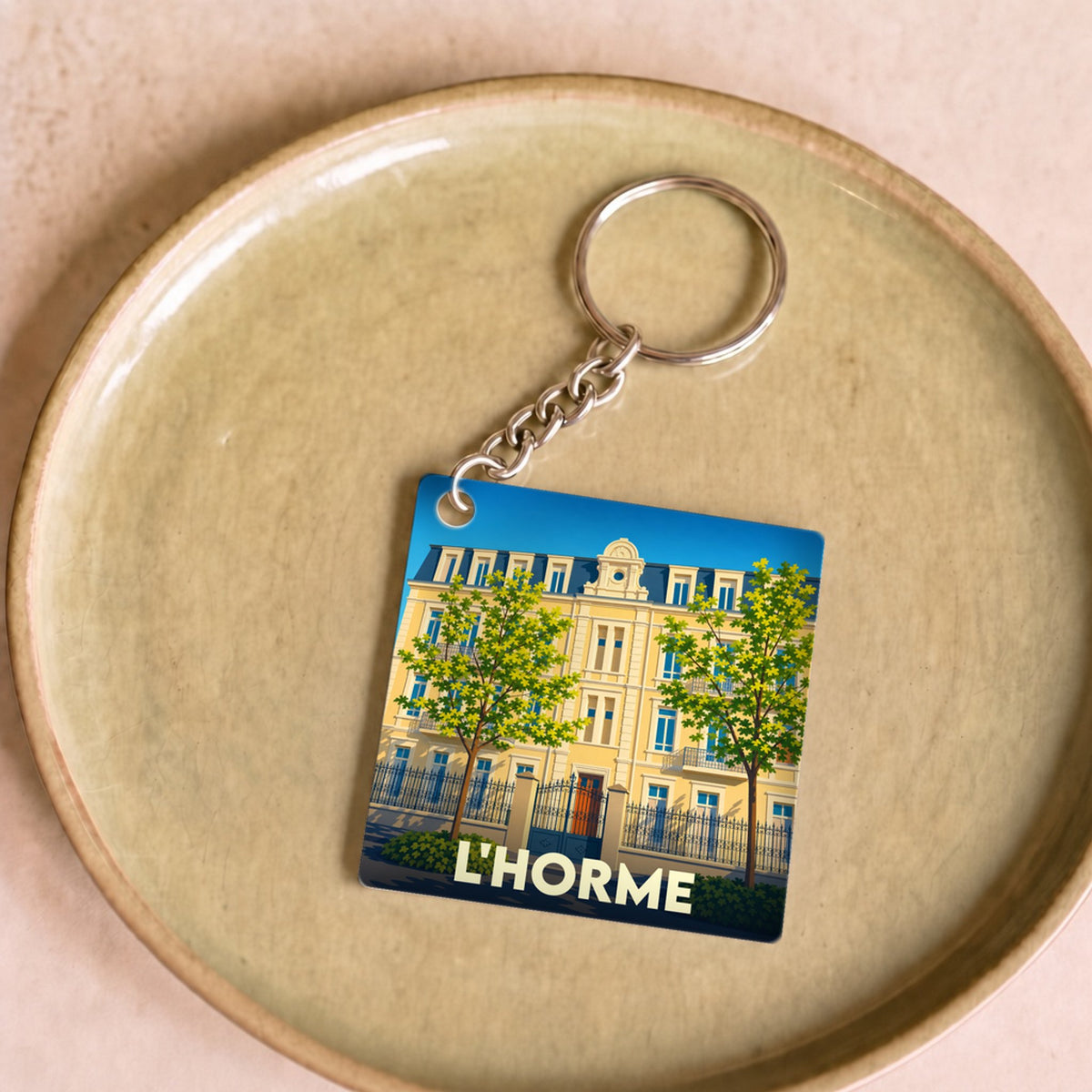Porte-clés souvenir de la ville de L'Horme avec une illustration stylisée d'un bâtiment classique.