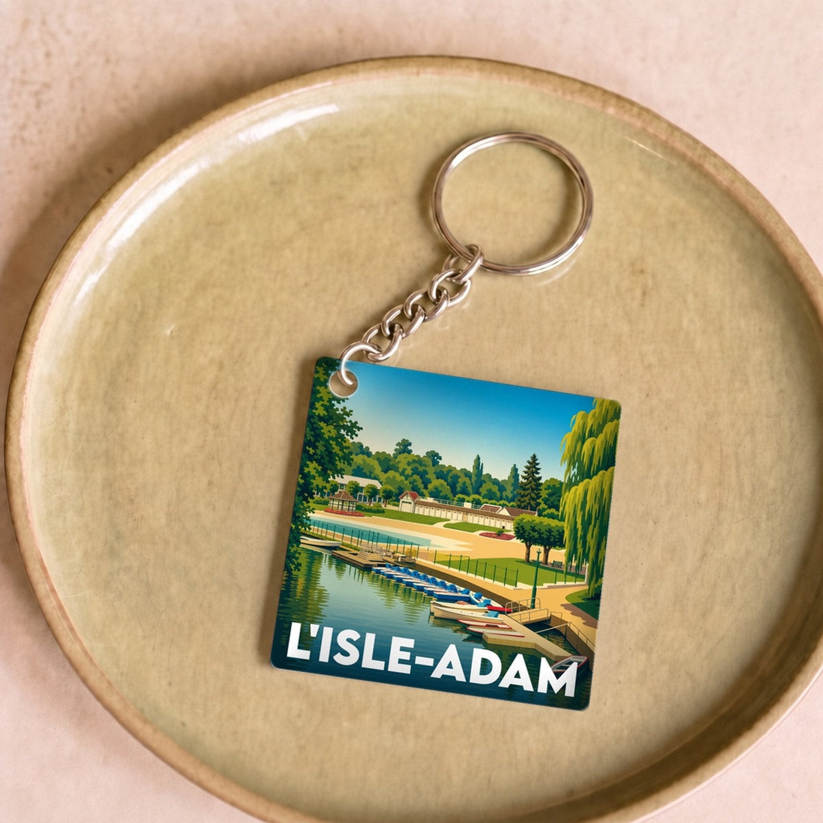 Porte-clés souvenir de la ville de L'Isle-Adam avec une illustration stylisée d'un bord de l'eau.