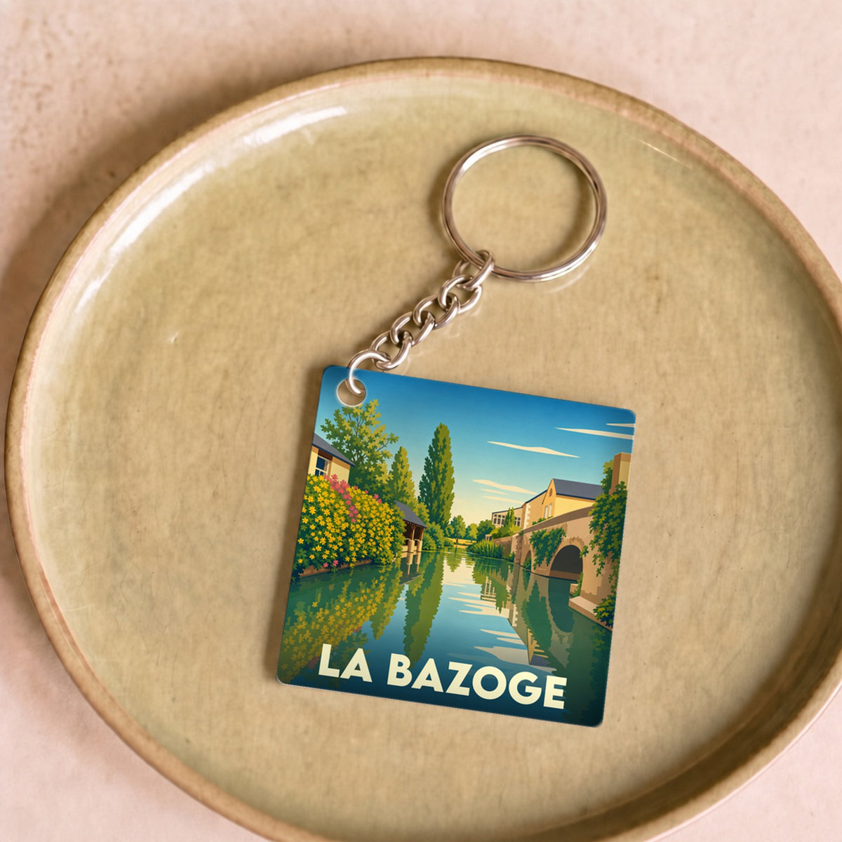 Porte-clés souvenir de la ville de La Bazoge avec une illustration stylisée d'un paysage fluvial.