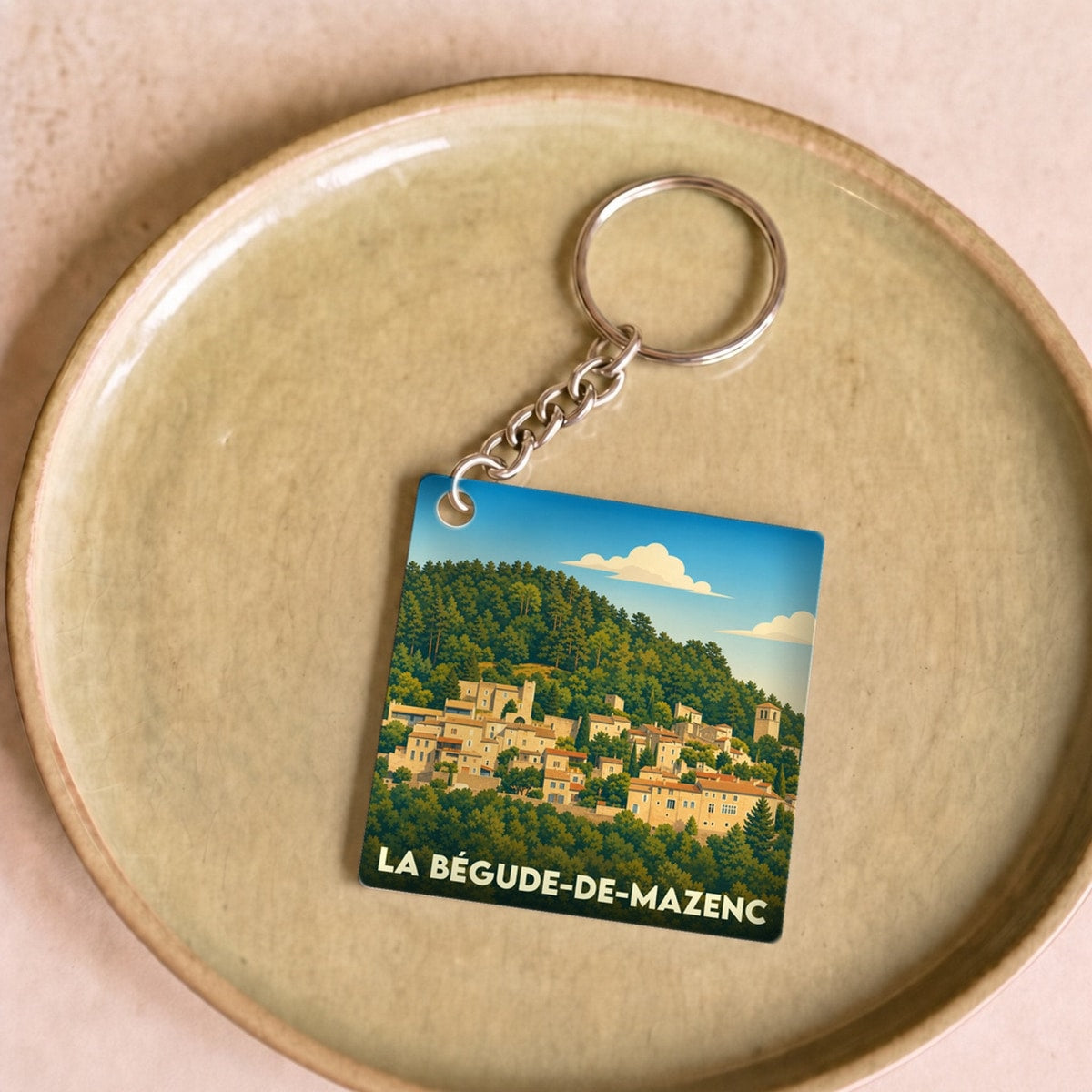 Porte-clés souvenir de la ville de La Bégude-de-Mazenc avec une illustration stylisée du village perché.