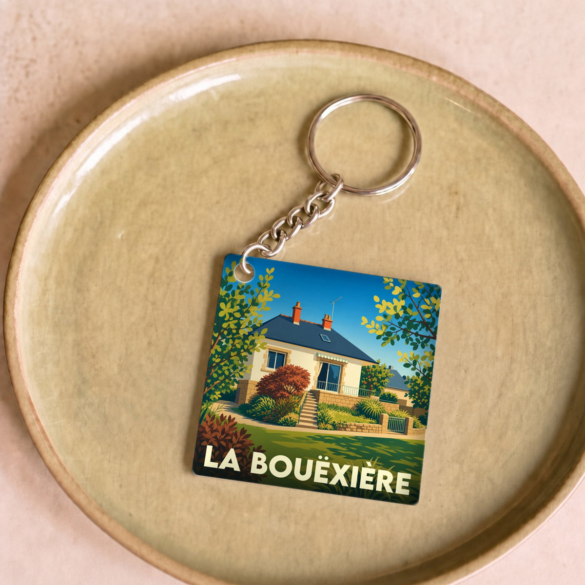 Porte-clés souvenir de la ville de La Bouëxière avec une illustration stylisée d'une maison fleurie.