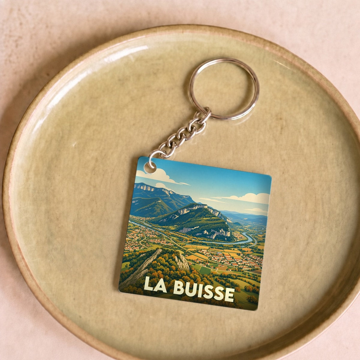 Porte-clés souvenir de la ville de La Buisse avec une illustration stylisée d'un paysage montagneux.