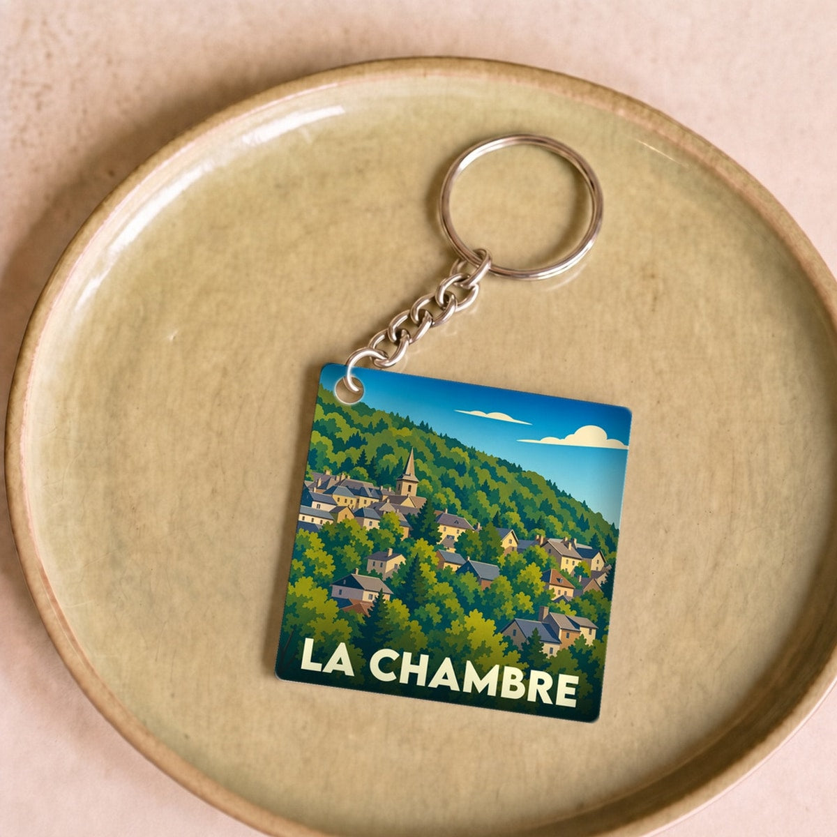 Porte-clés souvenir de la ville de La Chambre avec une illustration stylisée d'un village niché dans une colline verdoyante.