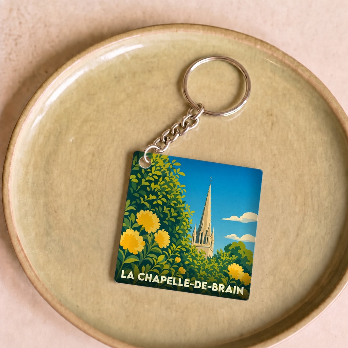 Porte-clés souvenir de la ville de La Chapelle-de-Brain avec une illustration stylisée d'un clocher et de fleurs.