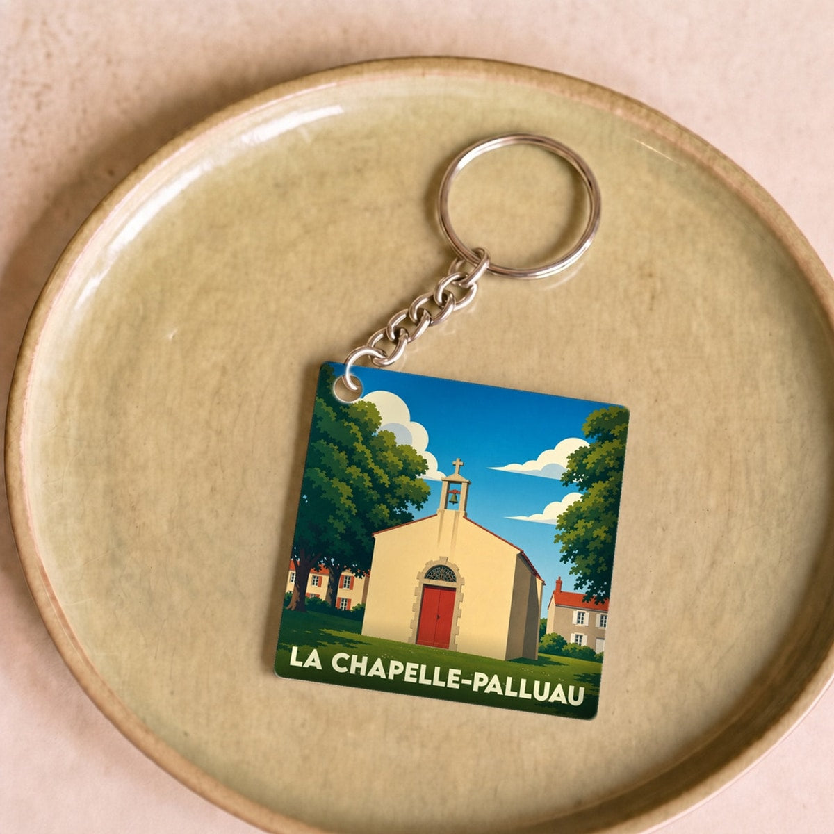 Porte-clés souvenir de la ville de La Chapelle-Palluau avec une illustration stylisée d'une petite chapelle sous un ciel bleu.