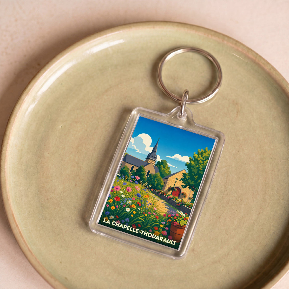 Porte-clés souvenir de la ville de La Chapelle-Thouarault avec une illustration colorée et stylisée d'un paysage fleuri.