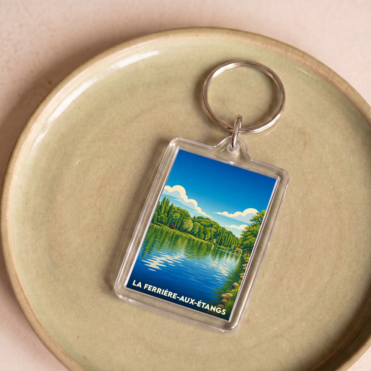Porte-clés souvenir de la ville de La Ferrière-aux-Étangs avec une illustration stylisée d'un lac bordé de forêt.