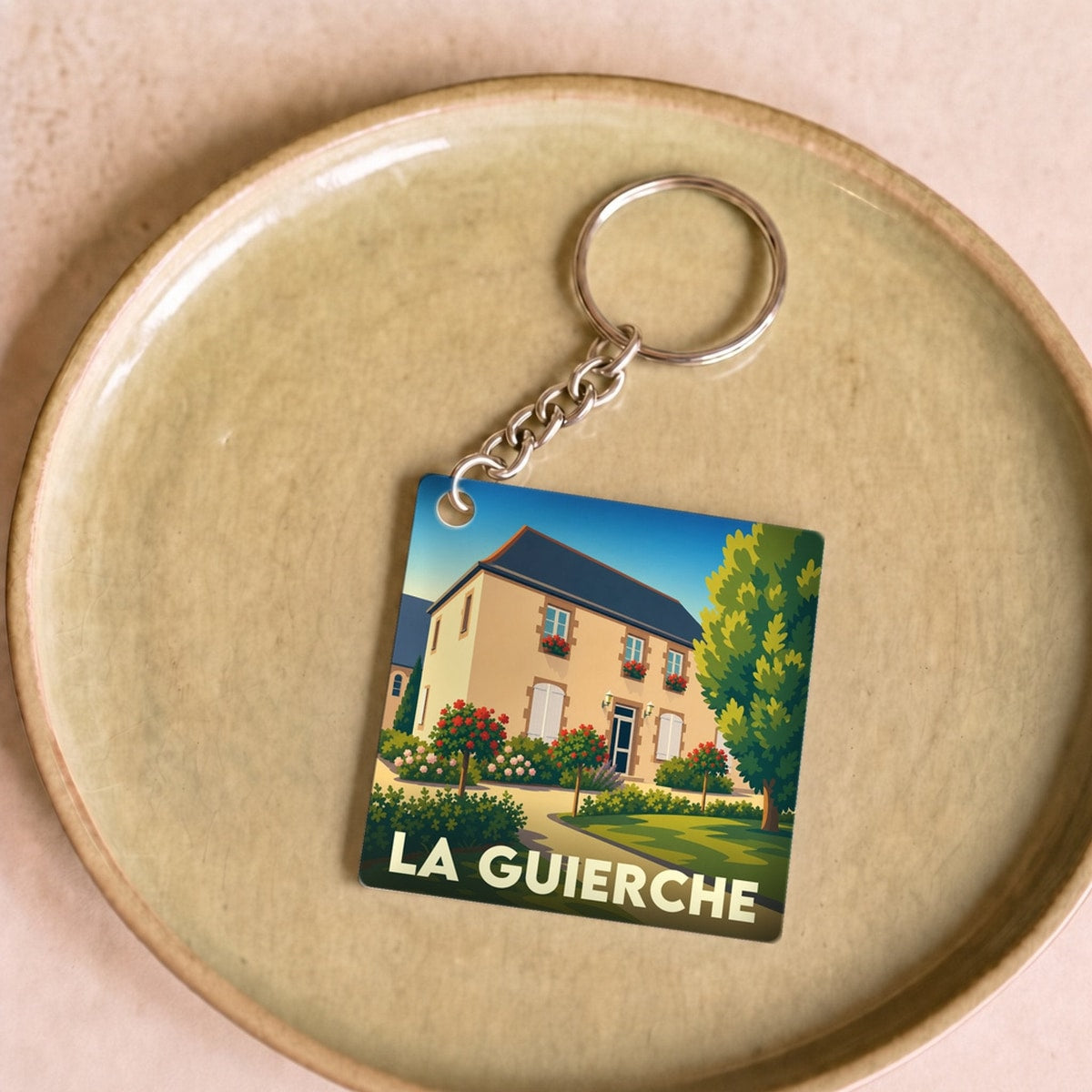 Porte-clés souvenir de la ville de La Guierche avec une illustration stylisée d'une maison fleurie.