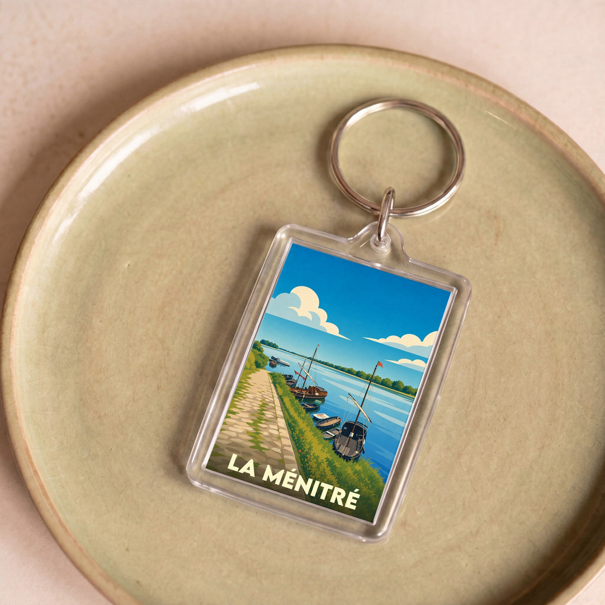 Porte-clés souvenir de la ville de La Ménitré avec une illustration stylisée de bateaux sur la Loire.