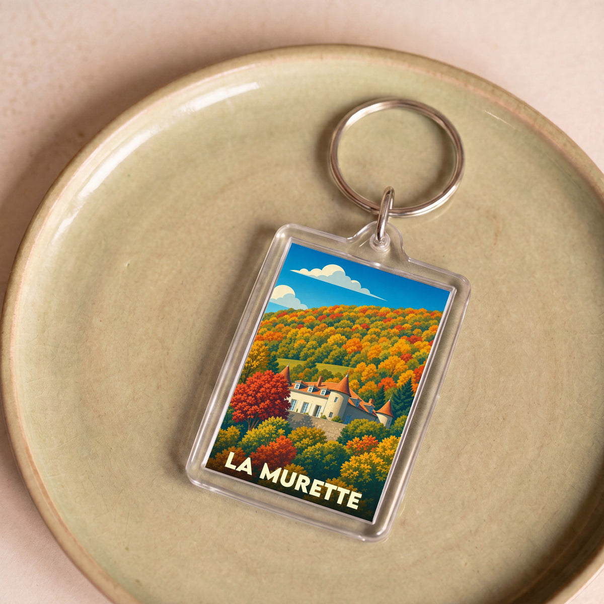 Porte-clés souvenir de la ville de La Murette avec une illustration stylisée d'un château entouré d'une forêt d'automne.