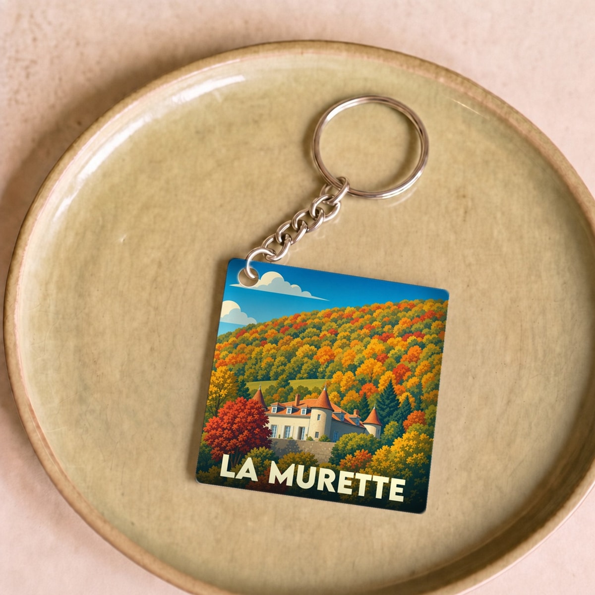 Porte-clés souvenir de la ville de La Murette avec une illustration stylisée d'un château entouré d'une forêt d'automne.