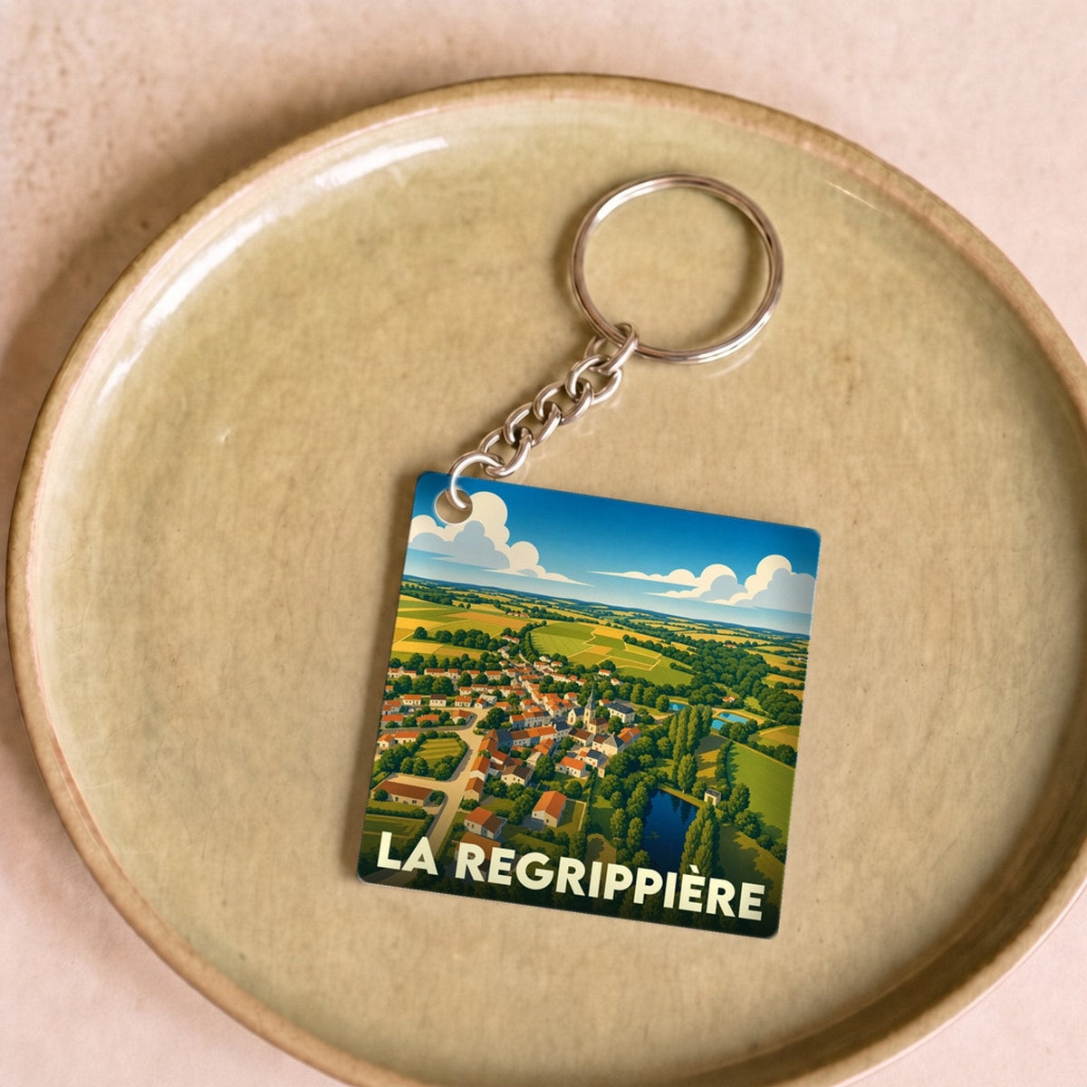 Porte-clés souvenir de la ville de La Regrippière avec une illustration stylisée de son paysage champêtre.