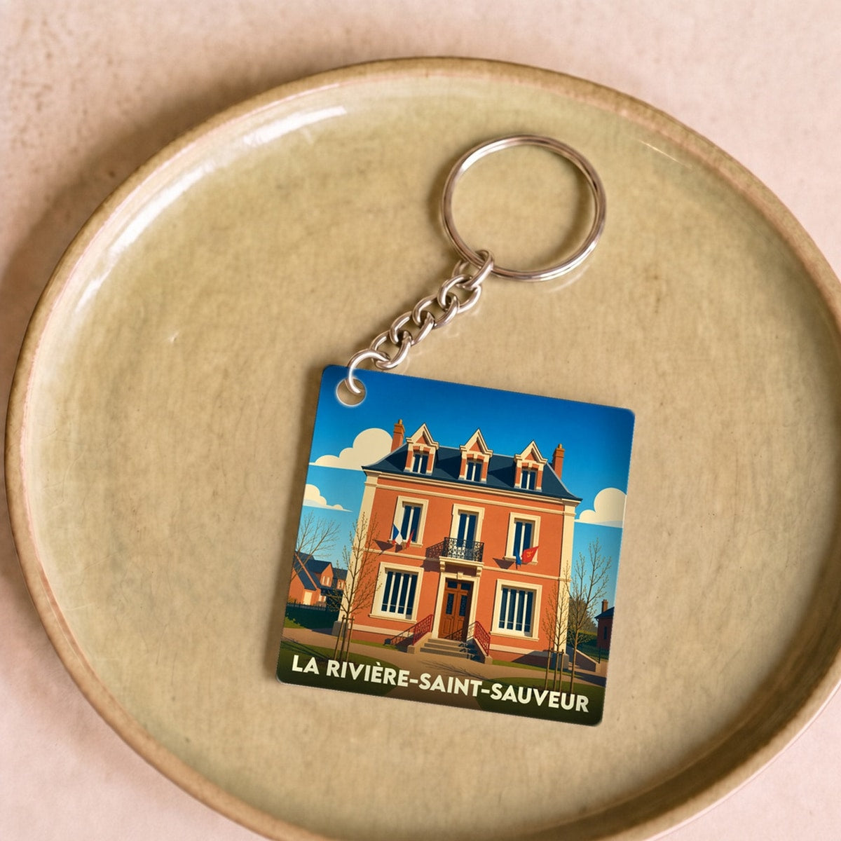 Porte-clés souvenir de la ville de La Rivière-Saint-Sauveur avec une illustration stylisée d'un bâtiment historique.