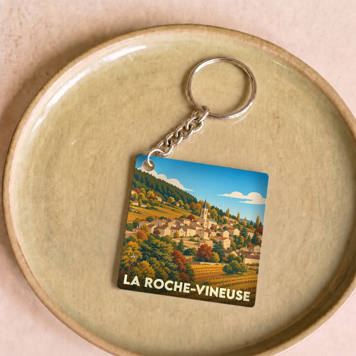 Porte-clés souvenir de la ville de La Roche-Vineuse avec une illustration stylisée de son paysage de vignes et de son village.