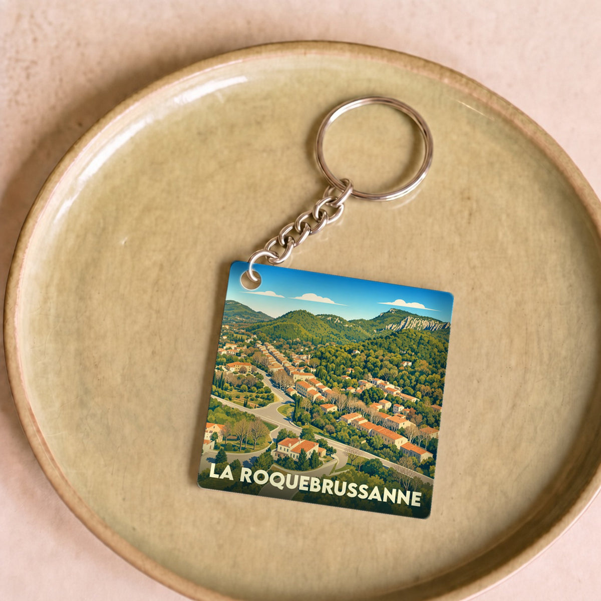 Porte-clés souvenir de la ville de La Roquebrussanne avec une illustration stylisée d'un paysage provençal.