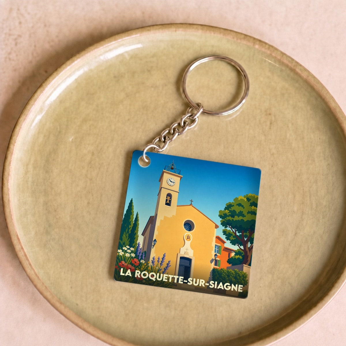 Porte-clés souvenir de la ville de La Roquette-sur-Siagne avec une illustration stylisée de son église provençale.