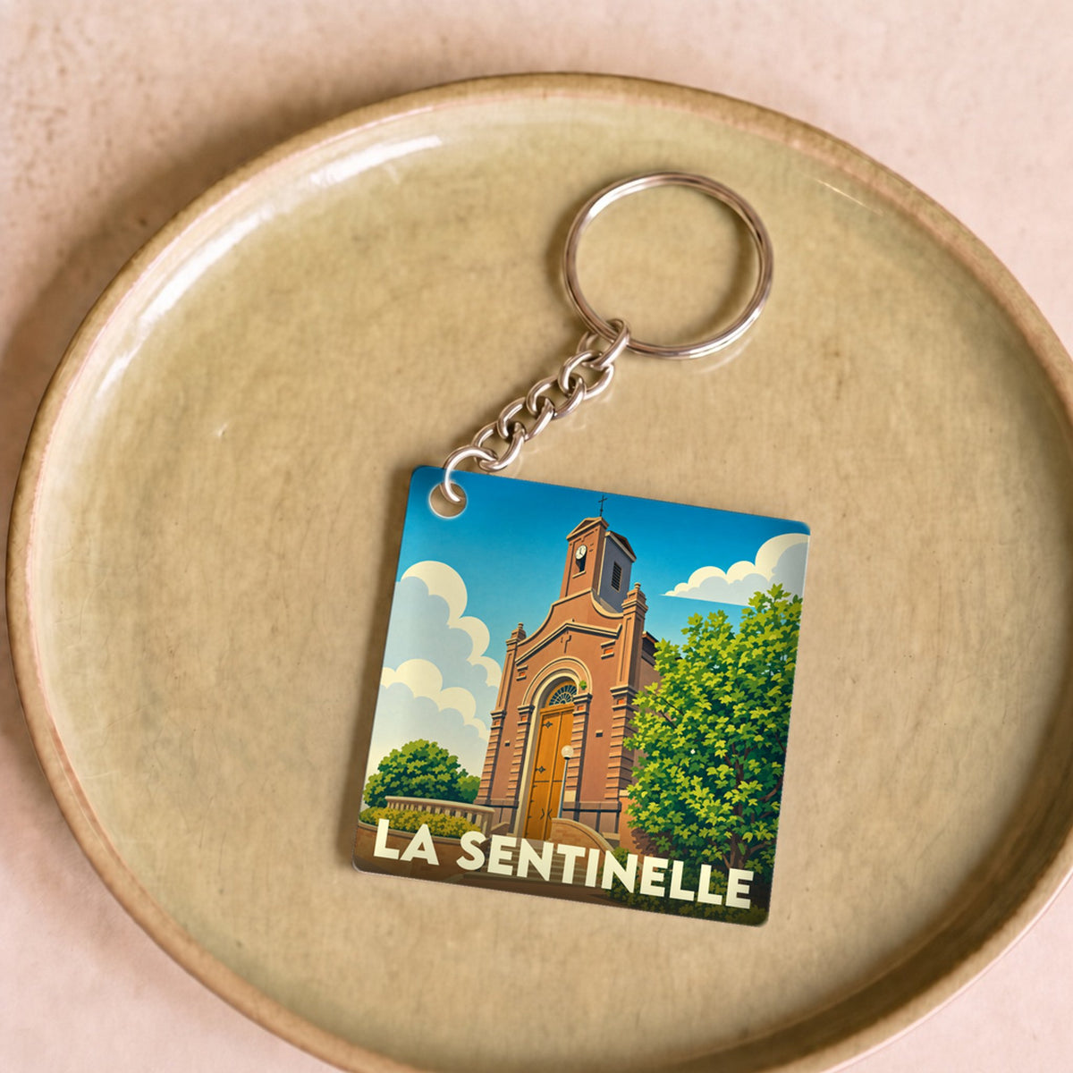 Porte-clés souvenir de la ville de La Sentinelle avec une illustration stylisée de son église.