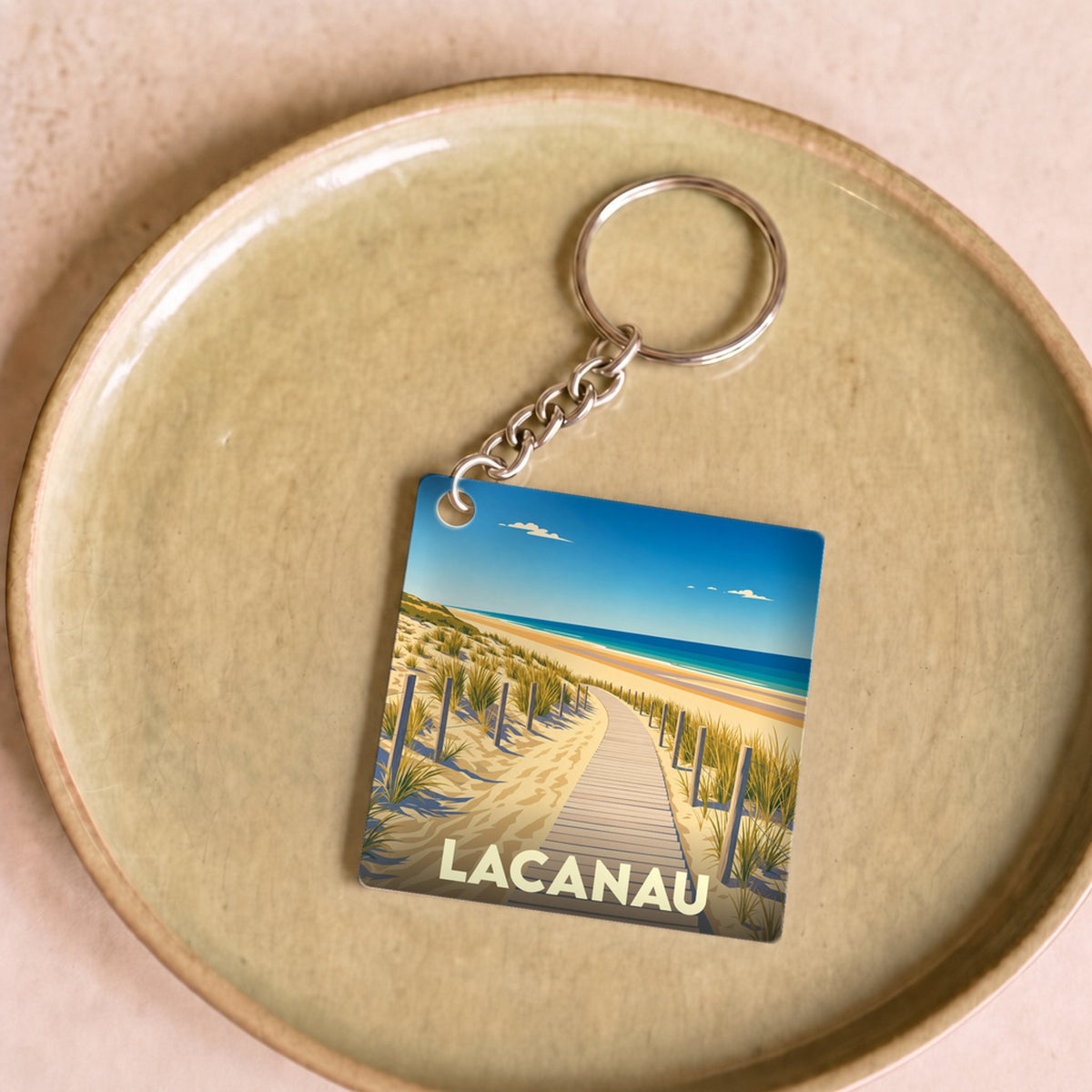 Porte-clés souvenir de la ville de Lacanau avec une illustration stylisée d'un chemin de plage.