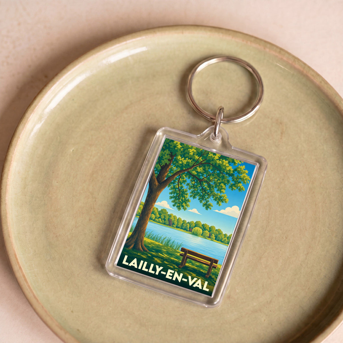 Porte-clés souvenir de la ville de Lailly-en-Val avec une illustration stylisée d'un paysage de bord d'eau.