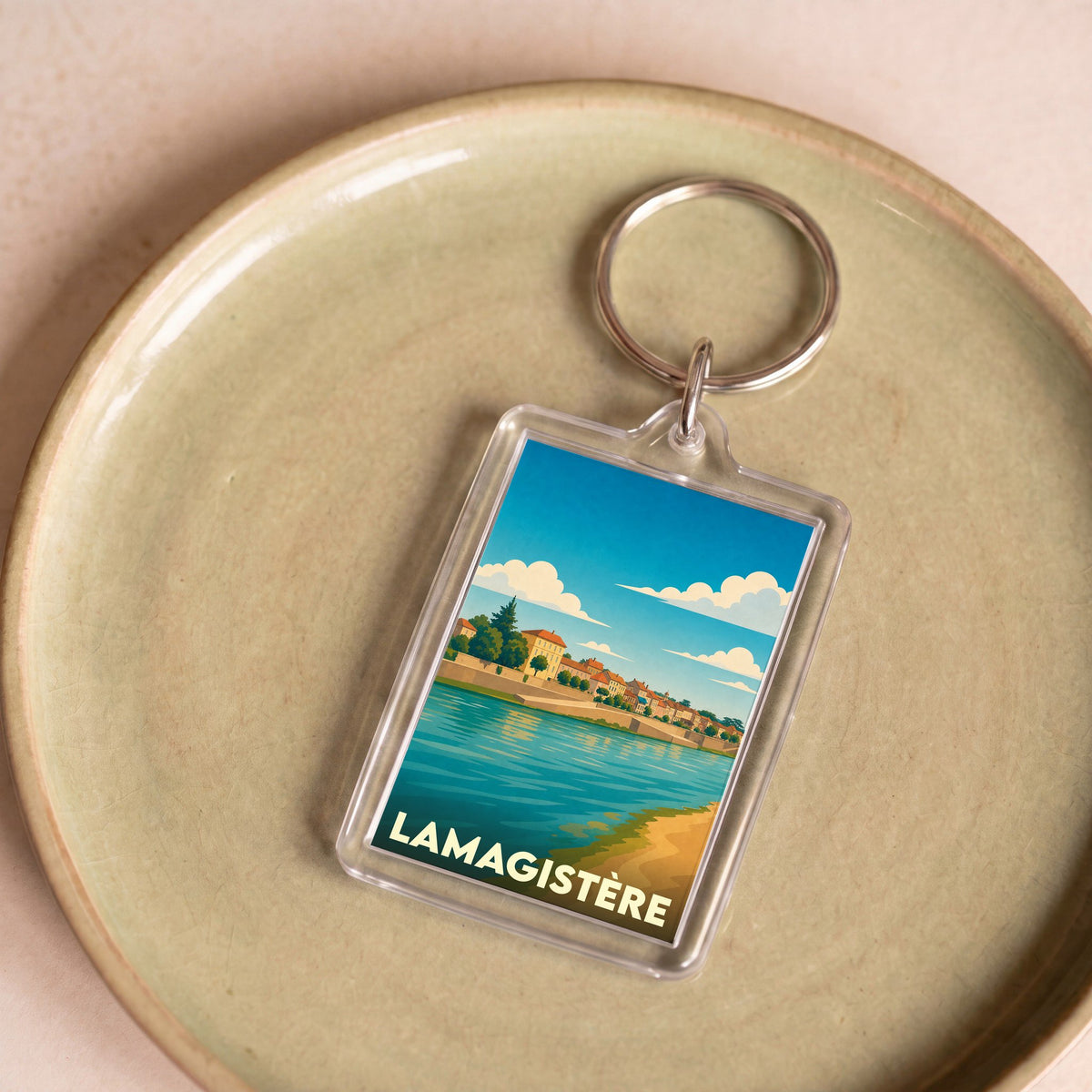 Porte-clés souvenir de la ville de Lamagistère avec une illustration stylisée d'un paysage de bord de rivière.