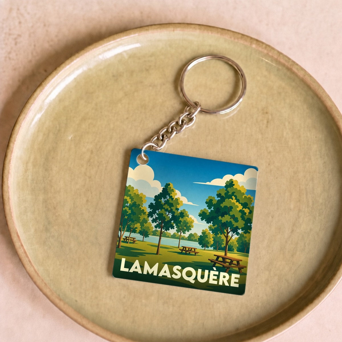 Porte-clés souvenir de la ville de Lamasquère avec une illustration stylisée d'un parc arboré.