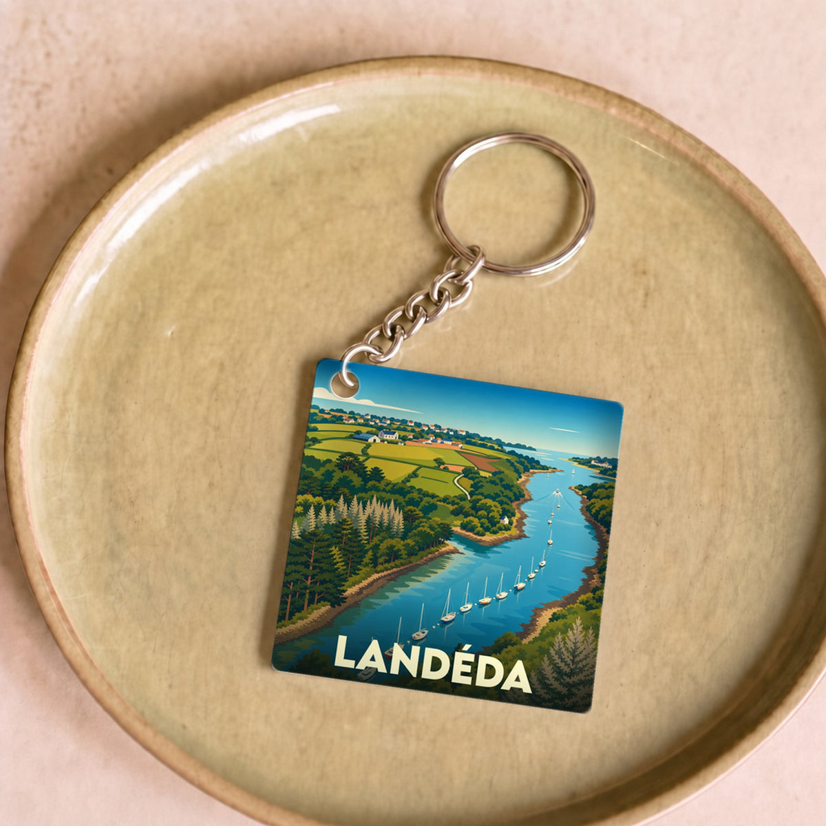 Porte-clés souvenir de la ville de Landéda avec une illustration stylisée d'un bras de mer bordé de collines verdoyantes.