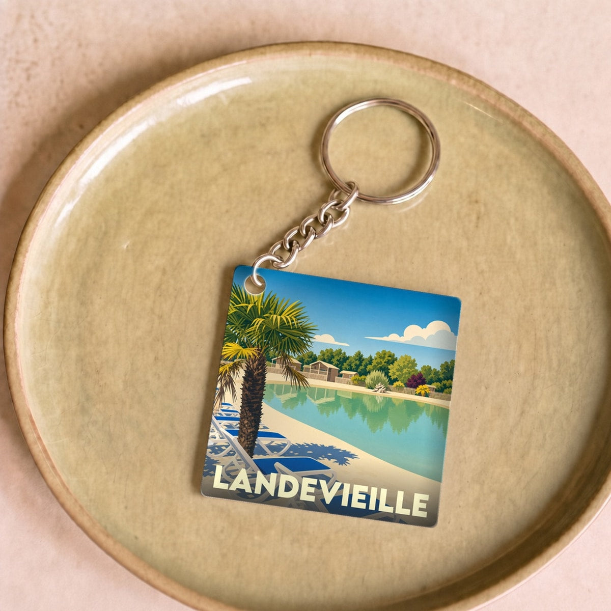 Porte-clés souvenir de la ville de Landevieille avec une illustration stylisée d'une piscine et de palmiers.