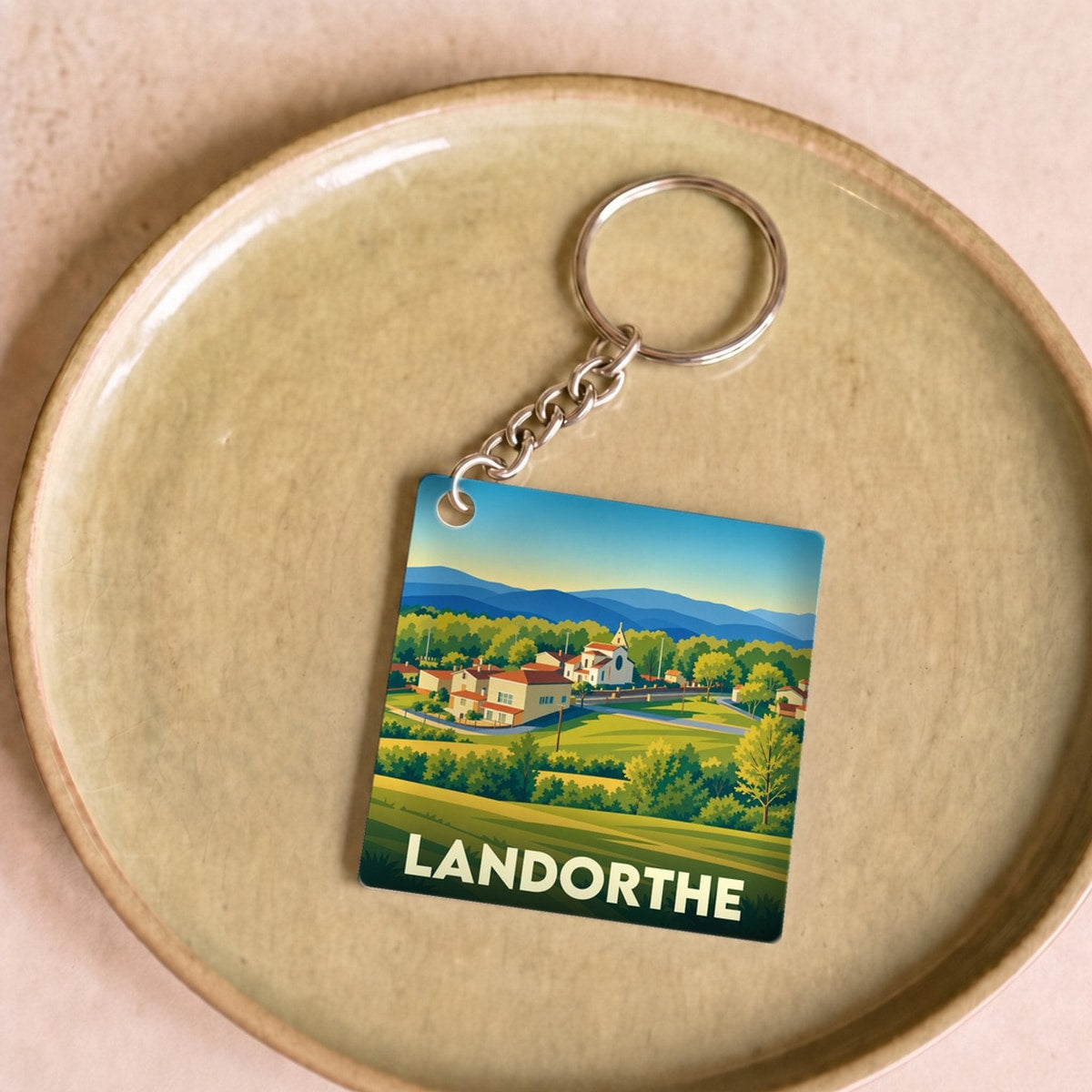 Porte-clés souvenir de la ville de Landorthe avec une illustration stylisée de son paysage vallonné.