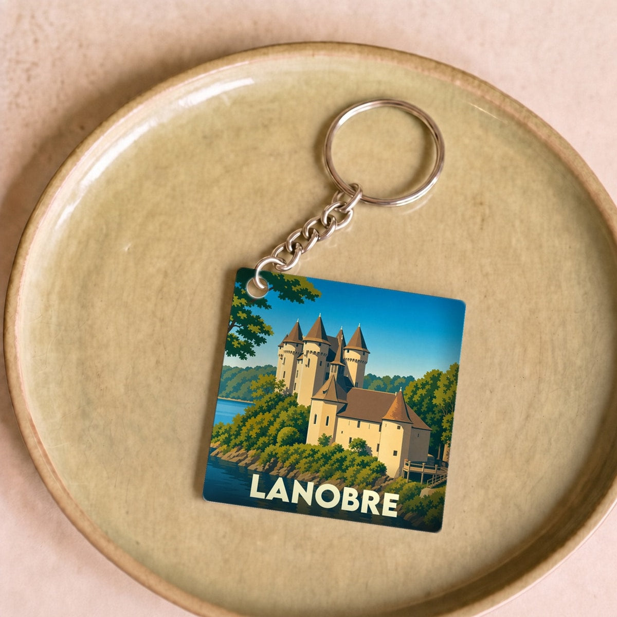 Porte-clés souvenir de la ville de Lanobre avec une illustration stylisée de son château au bord de l'eau.