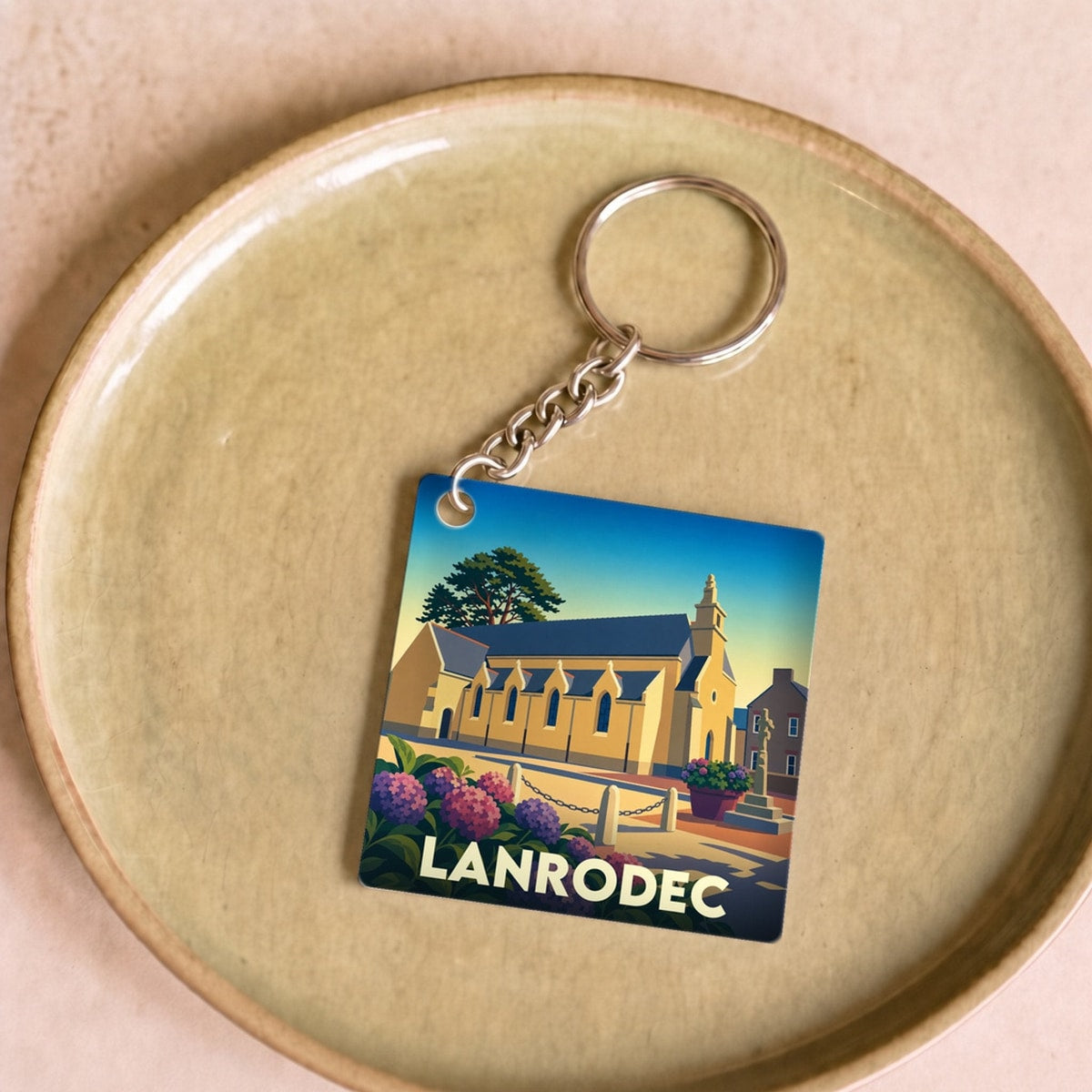 Porte-clés souvenir de la ville de Lanrodec avec une illustration stylisée de son église et de fleurs d'hortensias.