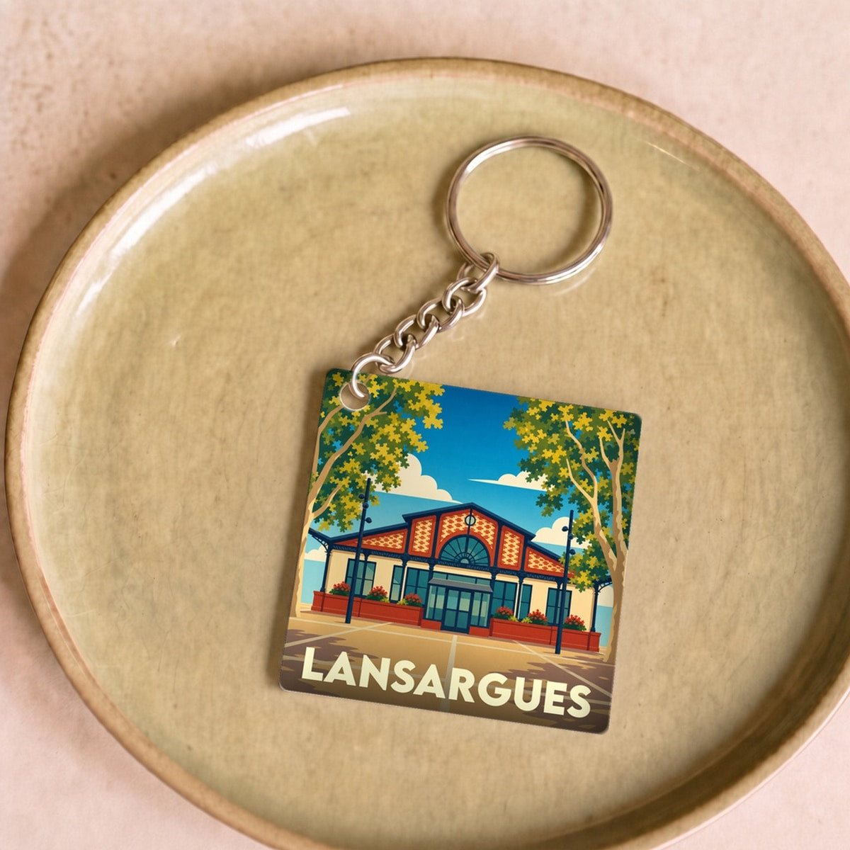 Porte-clés souvenir de la ville de Lansargues avec une illustration stylisée d'un bâtiment emblématique et de platanes.