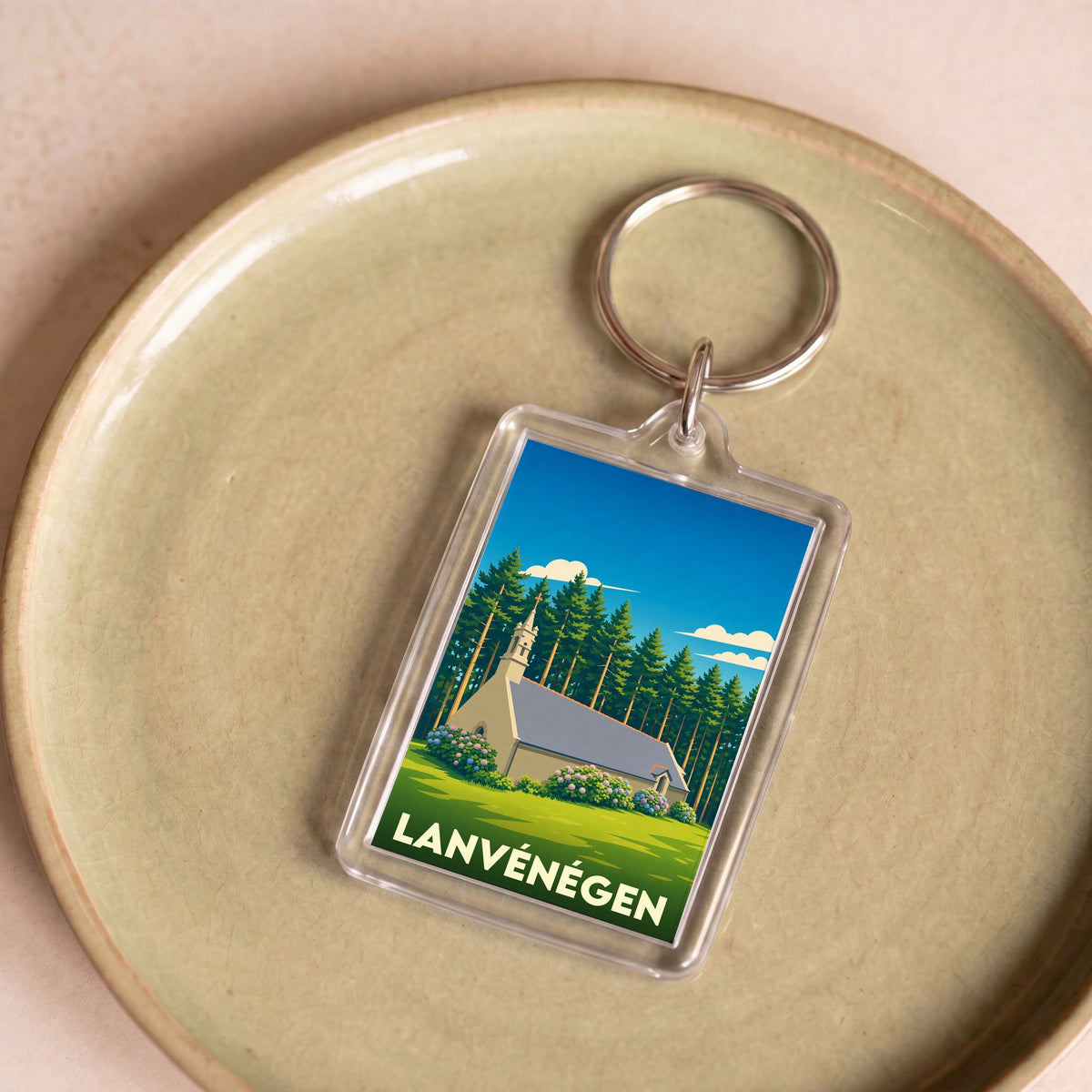 Porte-clés rectangulaire souvenir de la ville de Lanvénégen avec une illustration stylisée d'une chapelle en lisière de forêt.